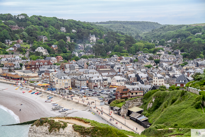 View from the cliffs looking down onto the town on Etretat. Many small buildings and many green trees