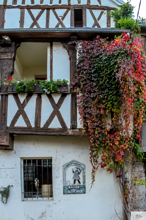 Close shot image of the outside of a building in France with flowers draping down the side