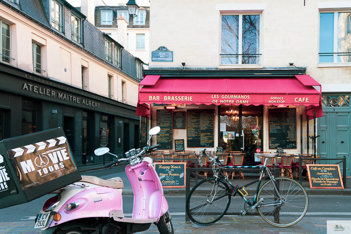 Pink Vespa parked next to a black bicycle outside of French Cafe