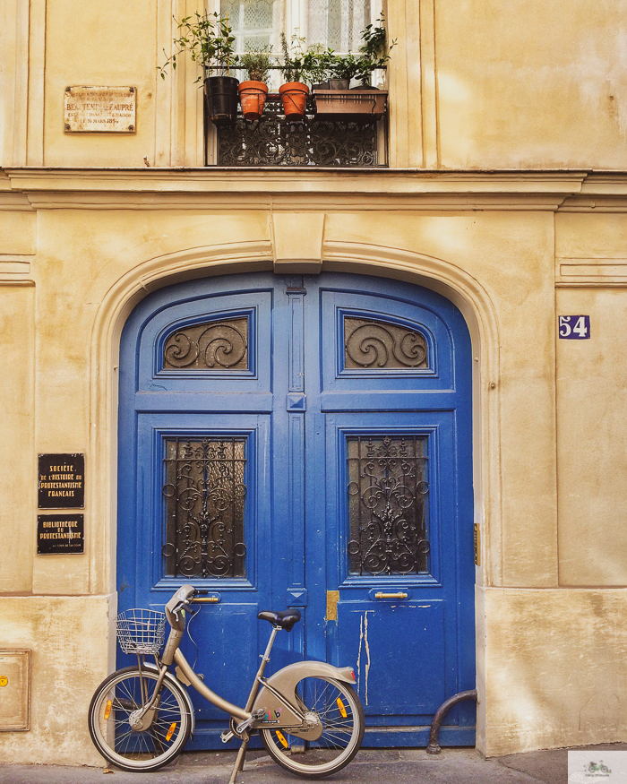 grey bike parked in front of two tall doors painted royal blue